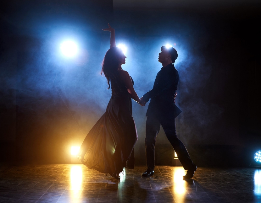 Skillful dancers performing in the dark room under the concert light and smoke. Sensual couple performing an artistic and emotional contemporary dance.